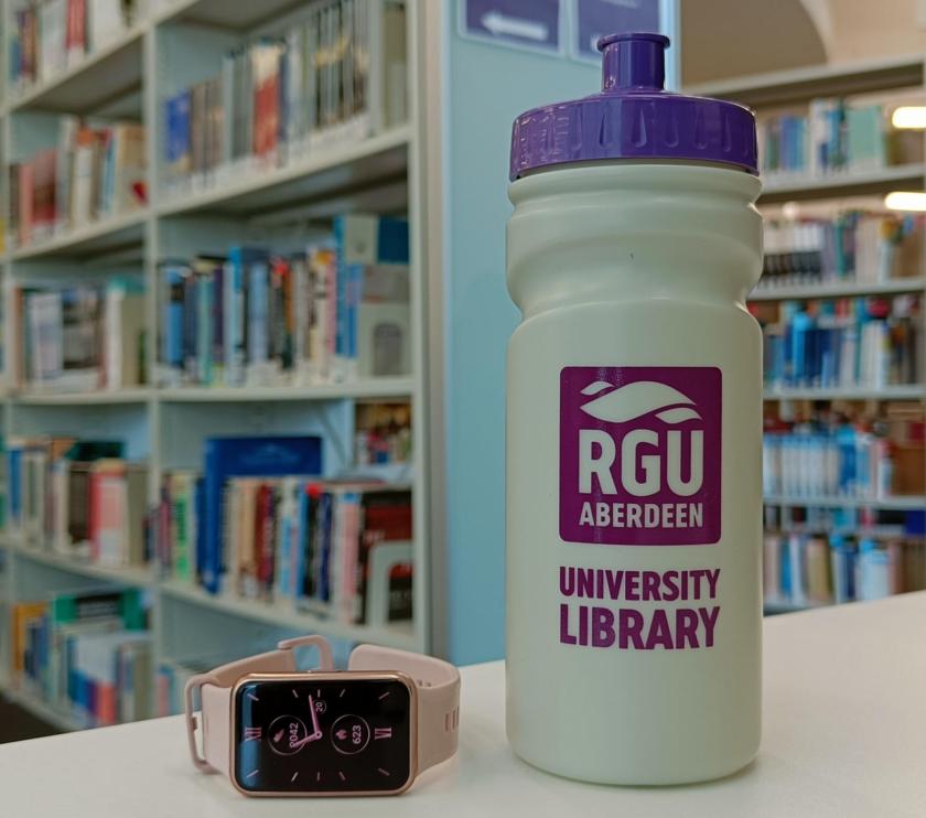 Watch and RGU LIbrary branded water bottle in front of library book shelves